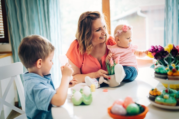 Mãe e filhos pintando ovos coloridos. A mãe, a criança e a criança em idade pré-escolar pintam e decoram o ovo de Páscoa.