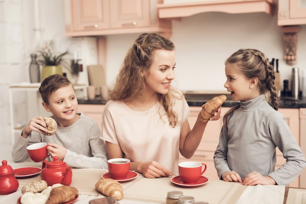 Mãe e filhos têm chá e croissants em casa.