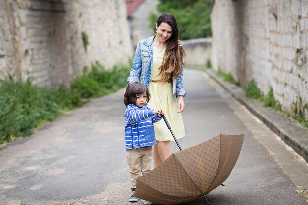 Mãe e garotinho bonito oriental brincando com guarda-chuva ao ar livre na cidade velha