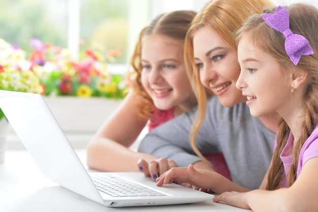 Mãe e meninas sentadas à mesa e usando laptop