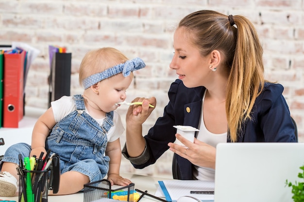 Mãe e mulher de negócios trabalhando com laptop em casa e brincando com sua filha.