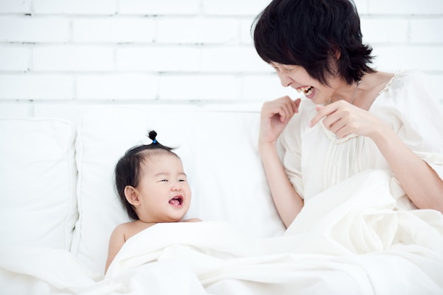 Mãe e o bebê estão sorrindo alegremente um para o outro em uma cadeira branca.