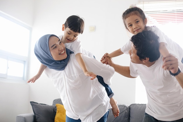 Mãe e pai asiáticos alegres carregam os filhos na sala de estar.