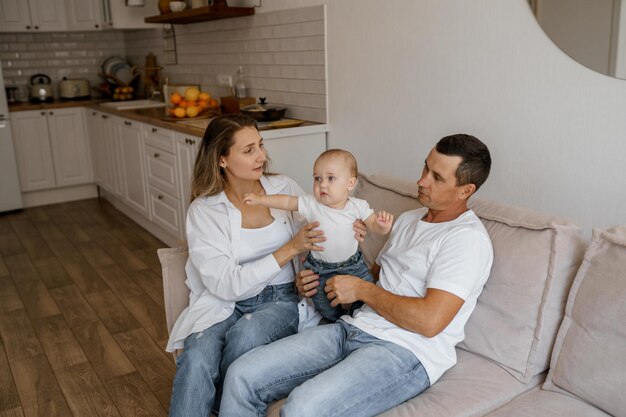 mãe e pai brincam no sofá com o filho perto das grandes janelas