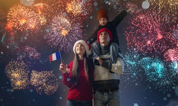 Mãe e pai com o filho nos ombros com roupas quentes e chapéu de Papai Noel A família comemora o ano novo olhando os fogos de artifício lá fora