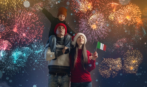 Mãe e pai com o filho nos ombros com roupas quentes e chapéu de Papai Noel A família comemora o ano novo olhando os fogos de artifício lá fora