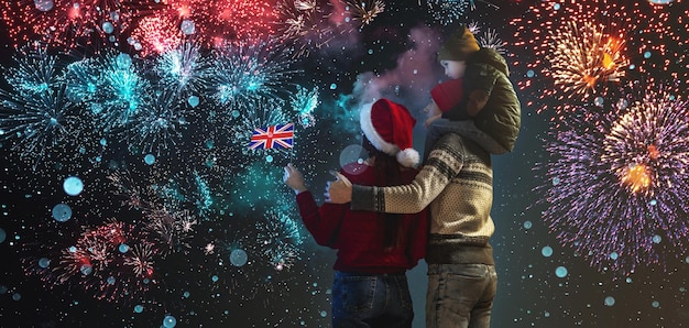 Mãe e pai com o filho nos ombros com roupas quentes e chapéu de Papai Noel A família comemora o ano novo olhando os fogos de artifício lá fora