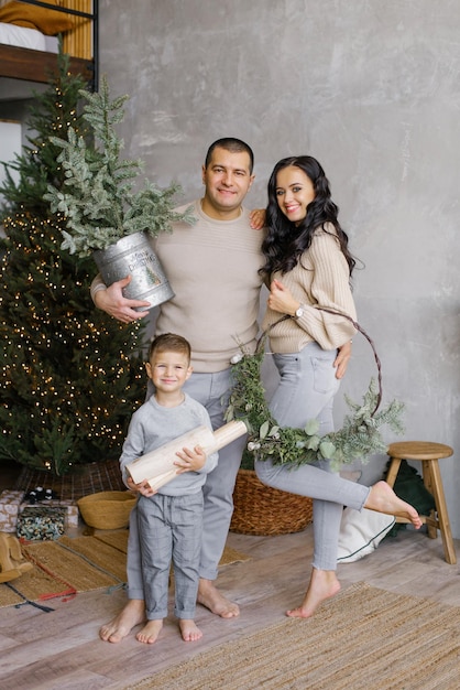 Mãe e pai sorridentes com seu filho pequeno estão parados na árvore de Natal decorada em casa Uma família feliz celebra o Natal ou o Ano Novo juntos