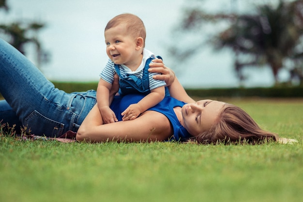 Mãe e seu filho sorridente brincam juntos, deitado gramado.