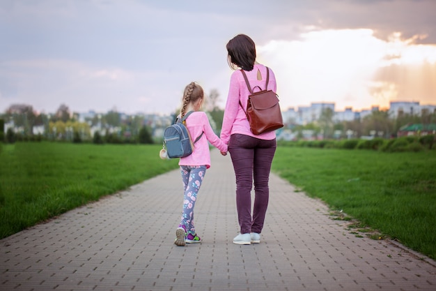 Mãe e seu pequeno dauther com mochila andando em dia de verão. Vista de trás.