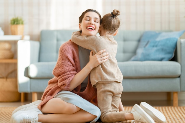 Mãe e sua filha estão brincando sorrindo e abraçando em casa