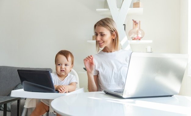 Mãe e sua filha pequena usam laptops e sentam-se nas mesas em casa Trabalho de maternidade e maternidade