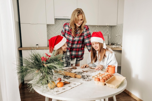 Mãe e suas filhas cozinham biscoitos de Natal ou pão de gengibre juntos cozinha familiar de comida festiva