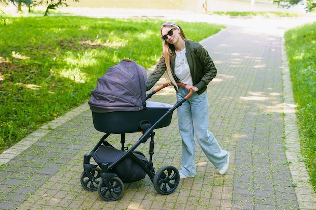 Mãe elegante caminha com um bebê em um carrinho no verão no parque