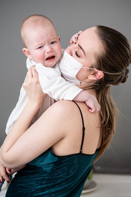 Mãe em máscara de proteção médica segura seu bebê nos braços durante a pandemia de coronovírus e covid-19