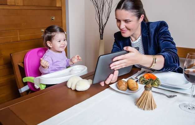 Mãe empresária e menina feliz olhando para um computador tablet sentado na mesa de um restaurante