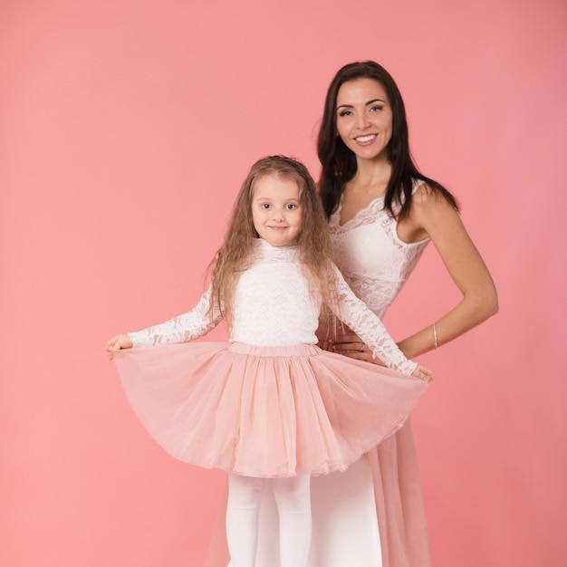 Mãe encantadora e filha sorridente em fundo rosa