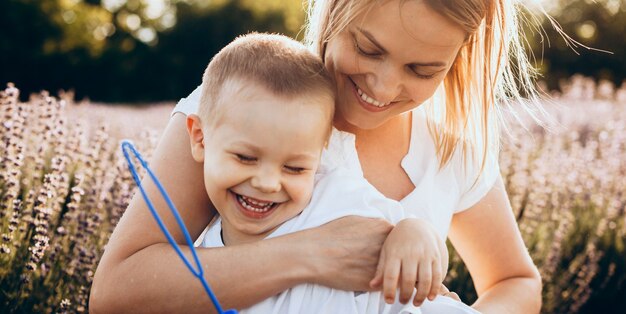 Mãe encantadora e filho sorrindo e se abraçando em um campo de lavanda fazendo balões com um brinquedo especial