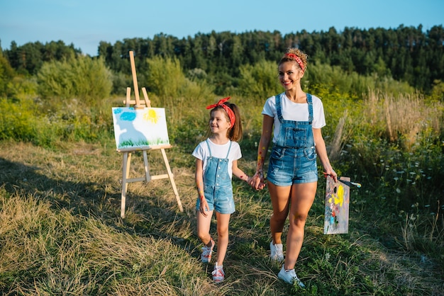 Mãe ensina filha a pintar no parque. natureza ensolarada, mãe e filha pintam um quadro em um parque, pintando uma criança, criatividade infantil.