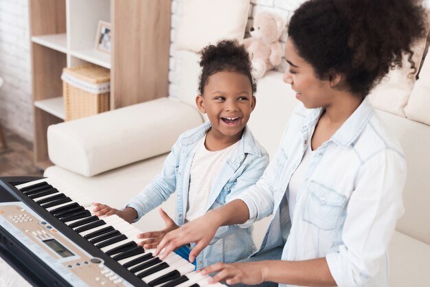 Mãe ensina uma menina a tocar piano.