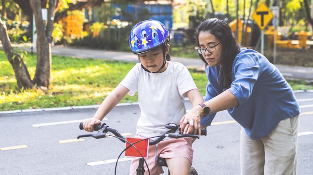 Mãe ensinando a filha a andar de bicicleta no parque. Família ao ar livre em um passeio de bicicleta.