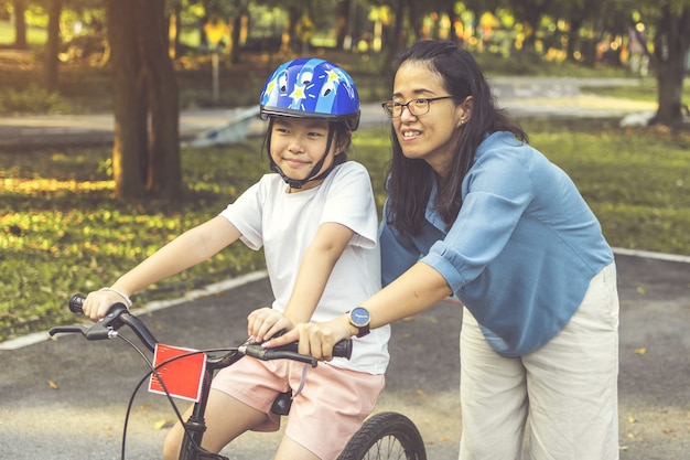 Mãe ensinando a filha a andar de bicicleta no parque. Família ao ar livre em um passeio de bicicleta.