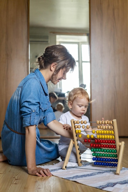 Mãe ensinando criança a contar com ábaco ecológico infantil multicolorido de madeira no chão