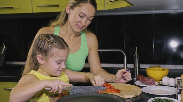 Foto mãe ensinando filha esperta aprendendo a cozinhar mistress crianças para cozinhar uma omelete frita de ovo napolitano de salsicha salame affumicato