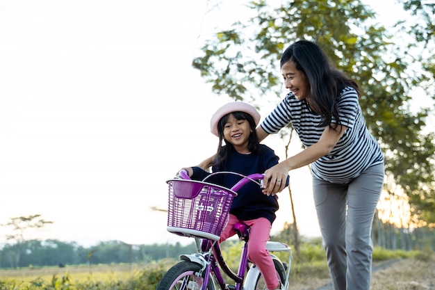 Mãe ensinando sua filha criança a aprender bicicleta