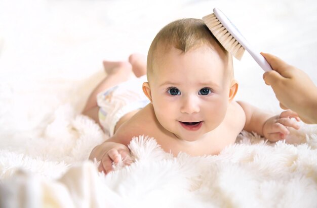 Mãe escovando o cabelo de um bebê bonito deitado na cama em casa