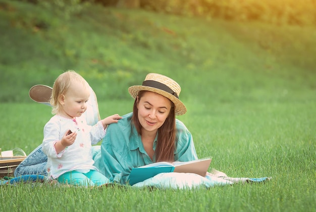 Mãe está lendo livro para menina deitada na grama do parque