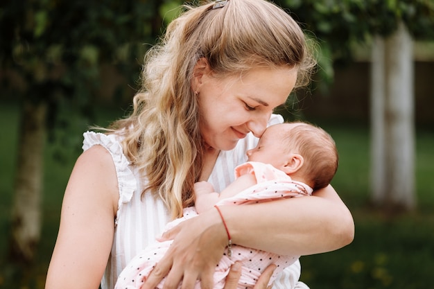 Mãe está segurando e abraçando a filha dela ao ar livre num dia de verão.