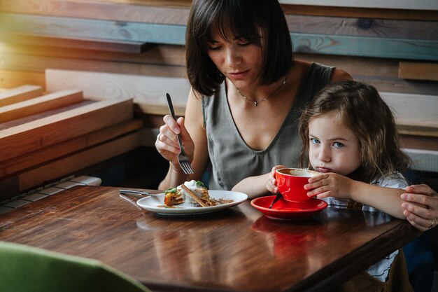 Foto mãe está sentada em um café com sua filha de dez anos, ela está comendo uma torta