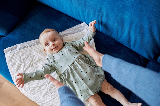 Foto mãe esticando as mãos para a filha recém-nascida no underpad no sofá. vista superior da bela criança infantil europeia usa um vestido elegante. conceito de maternidade e relacionamento familiar