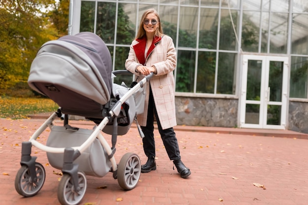 Mãe estilosa com carrinho no parque outono