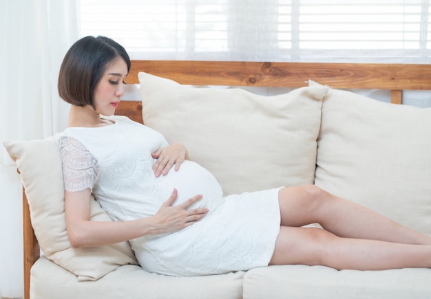 mãe expectante, sentada no sofá, tocando sua barriga