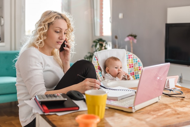 Mãe falando no telefone inteligente em casa, escritório