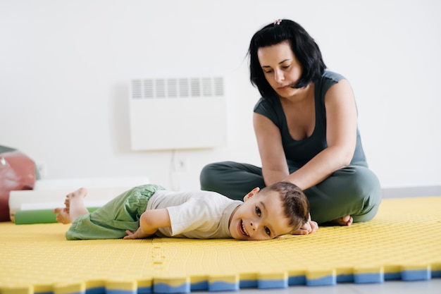 Foto mãe fazendo exercícios físicos brincando com menino deficiente