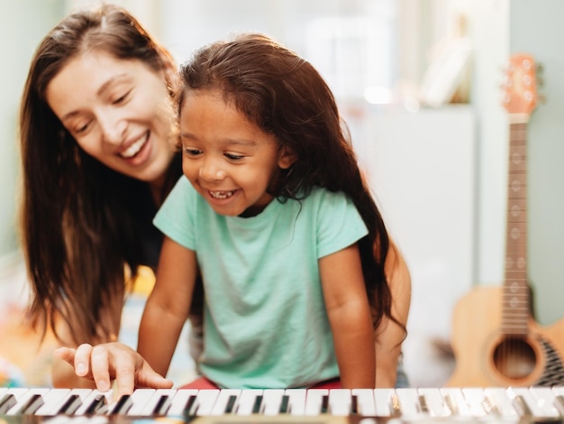 Mãe feliz a ensinar piano à filha em casa.