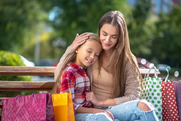 Mãe feliz abraçando a filha no banco do parque