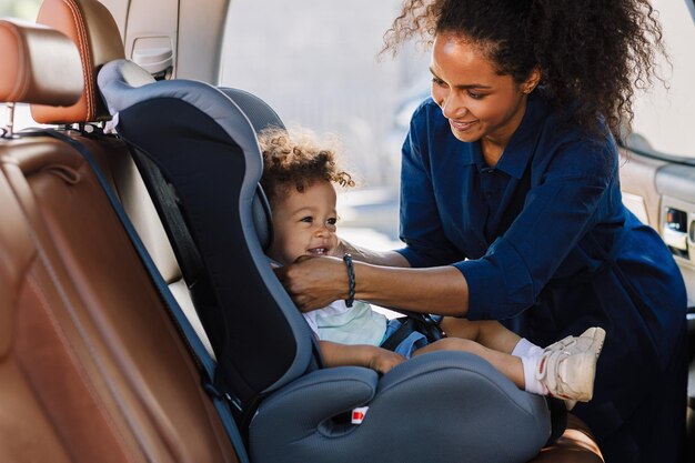 Mãe feliz ajustando o cinto em uma cadeirinha de bebê Garotinho sorrindo enquanto sua mãe preparava sua cadeirinha para a viagem