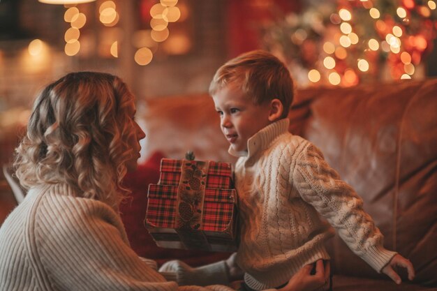 Mãe feliz autêntica e sincera passa tempo com seu filho alegre no chalé de madeira decorado de Natal