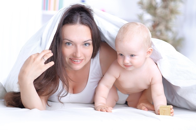 mãe feliz brinca com o bebê deitado na cama. o conceito de educação