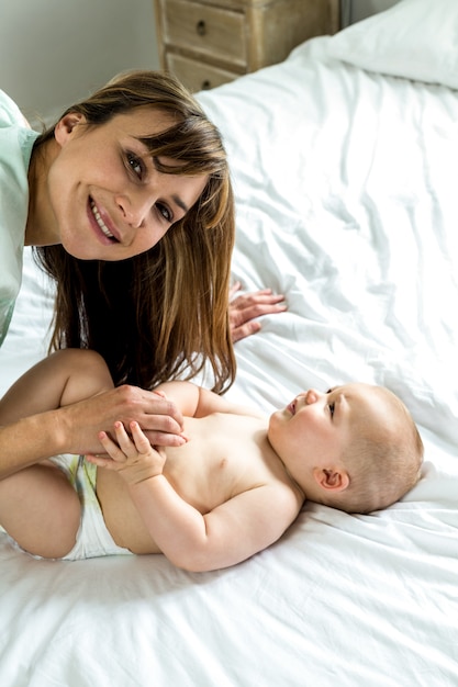 Mãe feliz, brincando com menino bonito na cama