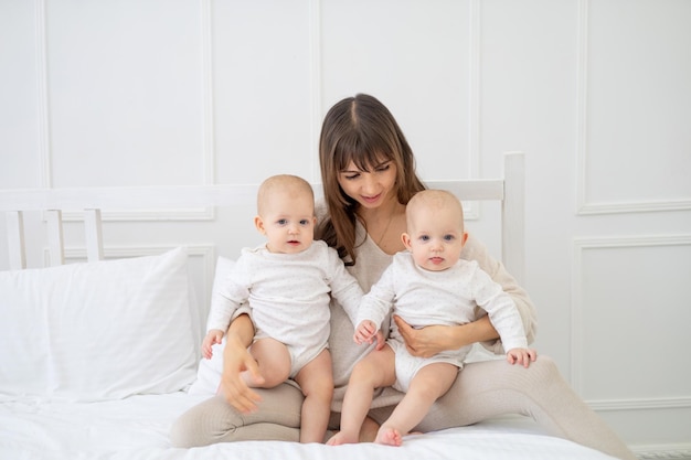 Mãe feliz com dois bebês gêmeos em casa na cama abraçando e beijando uma jovem família feliz com a maternidade das crianças