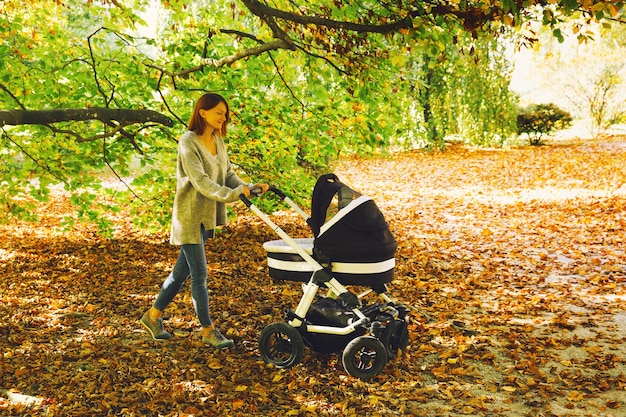 Foto mãe feliz com seu bebê recém-nascido na natureza criança dormindo em um carrinho ao ar livre