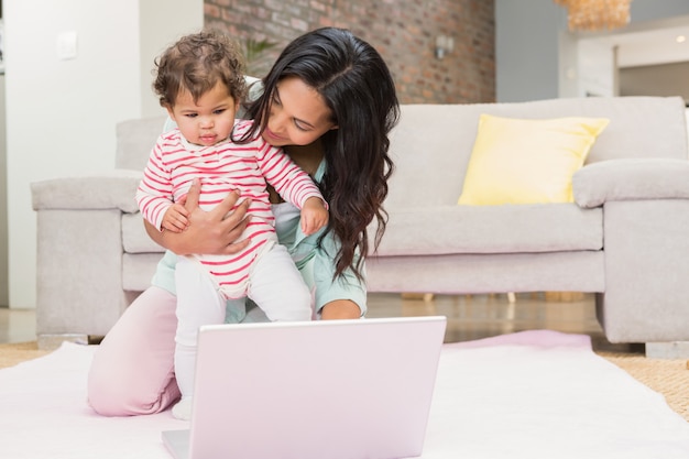 Mãe feliz com seu bebê usando laptop no tapete na sala de estar