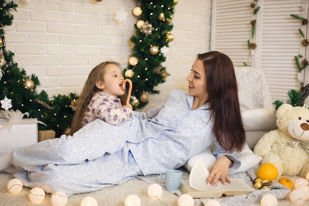 Mãe feliz com sua filha brincando perto da árvore de Natal