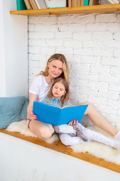 Mãe feliz com sua filha lendo um livro e sorrindo enquanto está sentada no chão da sala de estar