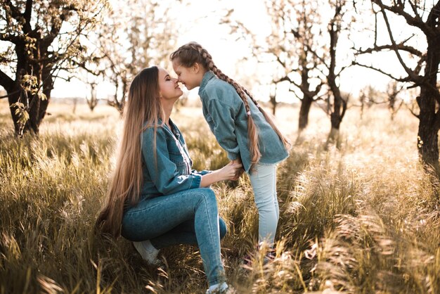 Mãe feliz com uma garota sorridente e vestindo roupas jeans juntas no prado